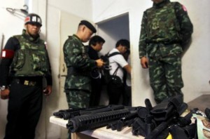 Soldiers stand next to a cache of weapons found in an derelict building where military forces say an explosive device was thrown on to anti-government protesters
