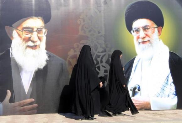 Iraqi women walk past a poster depicting images of Shi'ite Iran's Supreme Leader Ayatollah Ali Khamenei at al-Firdous Square in Baghdad