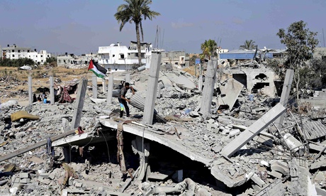 A Palestinian flag flutters as a man searches the remains of his house