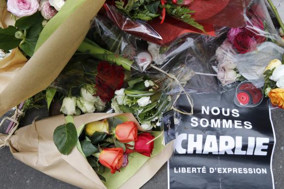 A sign which reads in French,"We are Charlie. Freedom of Expression" is placed on flowers as people continue to pay tribute to the shooting victims in front of the offices of weekly satirical newspaper Charlie Hebdo in Paris