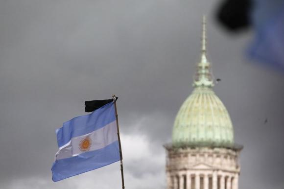 A black ribbon is seen on a national flag with the National Congress building in the background during a silent march to honour late state investigator Alberto Nisman in Buenos Aires February 18, 2015. CREDIT: REUTERS/ENRIQUE MARCARIAN